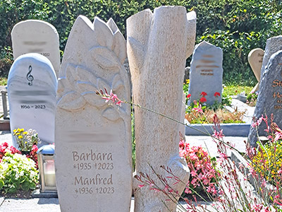 Grabstein mit floralen Elementen und Baumstamm aus Stein